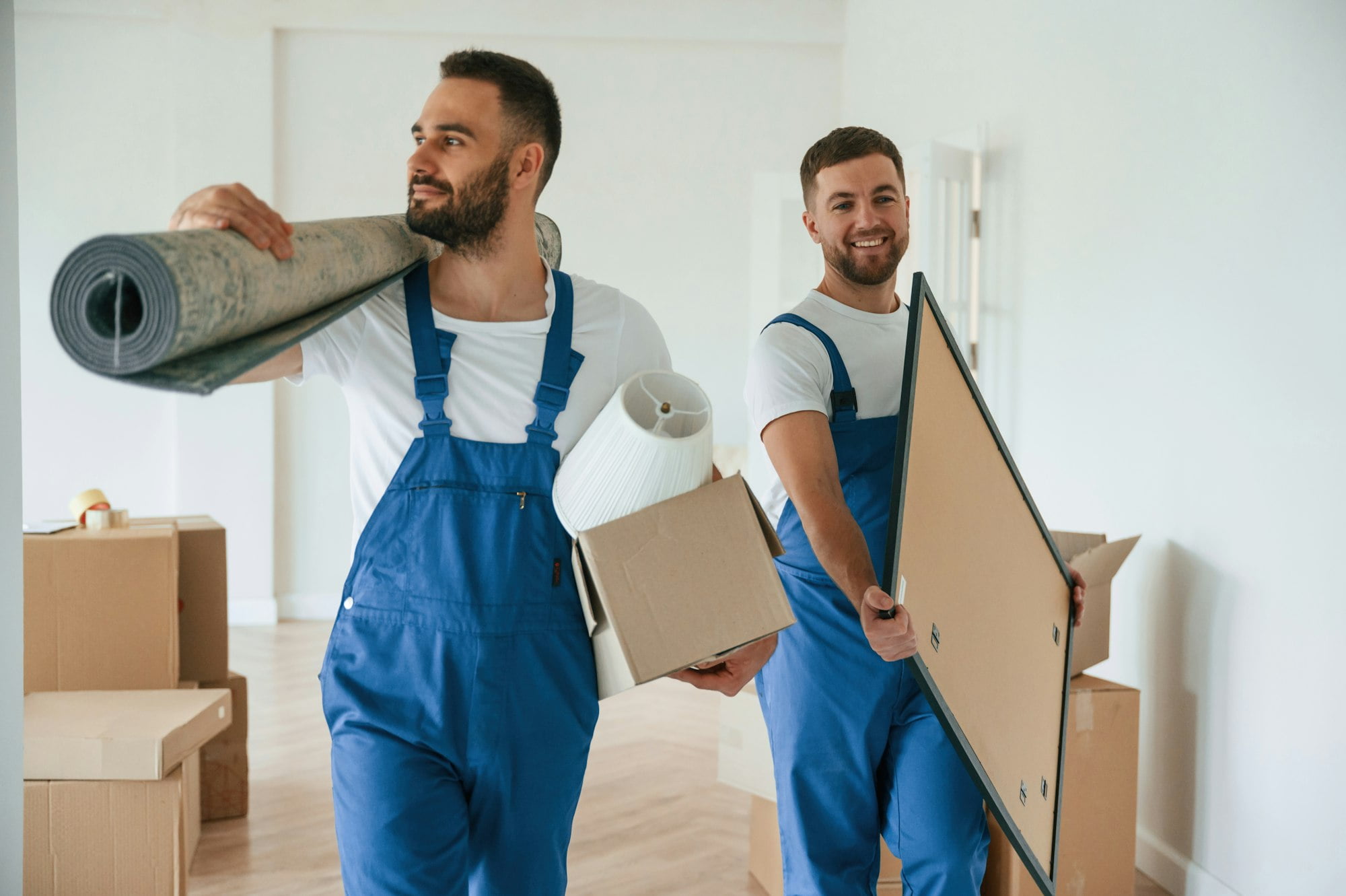 Mat and painting in hands. Two moving service employees in a room